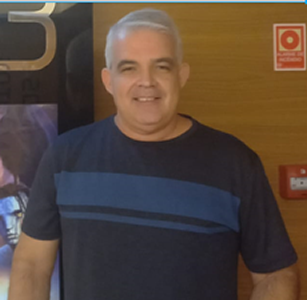 Foto de um Homem branco, cabelos grisalhos, alto, usando uma camisa azul e calça jeans